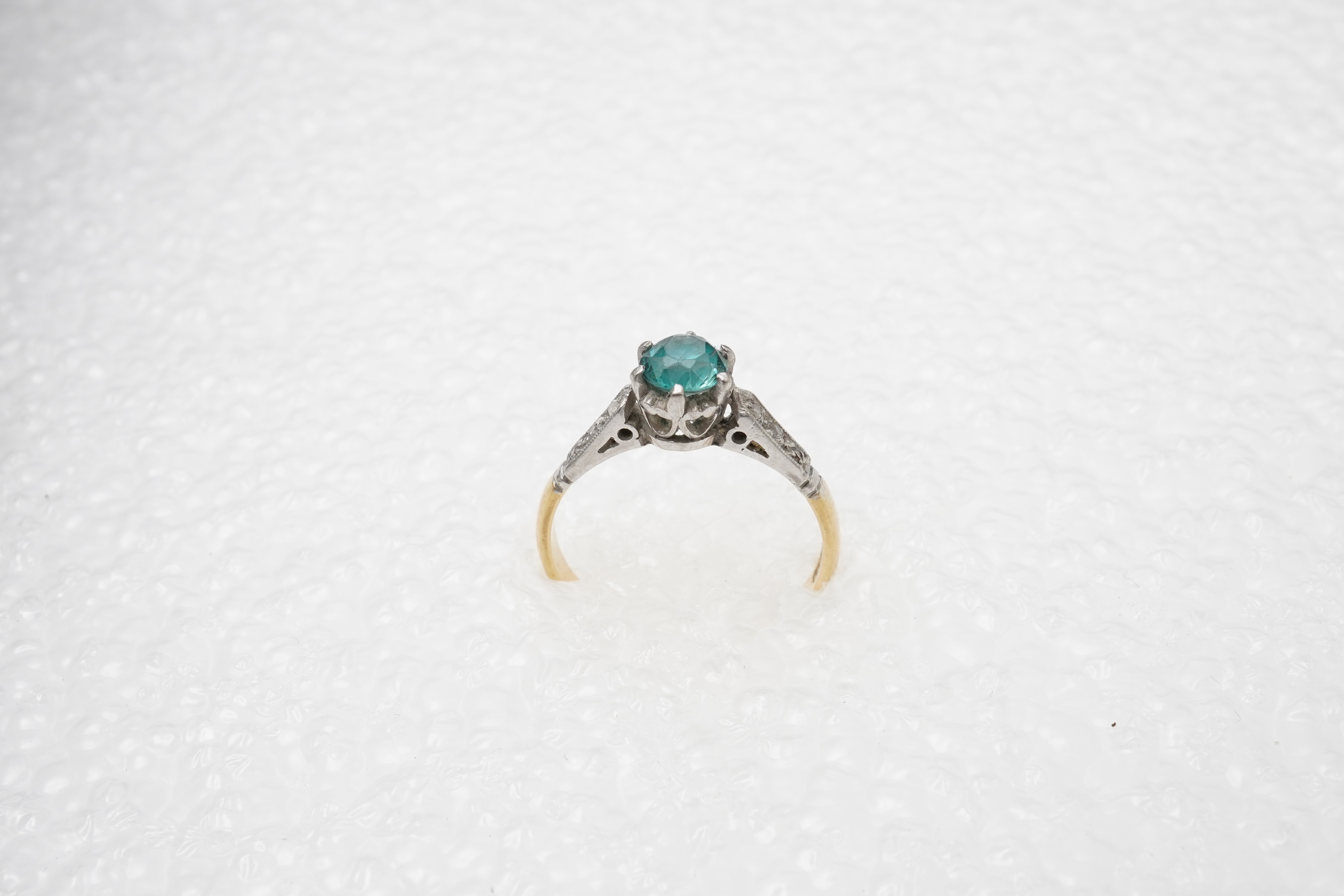 A zircon and diamond ring, mid 20th century, claw-set with a brilliant-cut blue zircon measuring approximately 5mm diameter, to shoulders set with rose-cut diamonds, mounted in gold, size N, stamped 18CT, gross weight ap